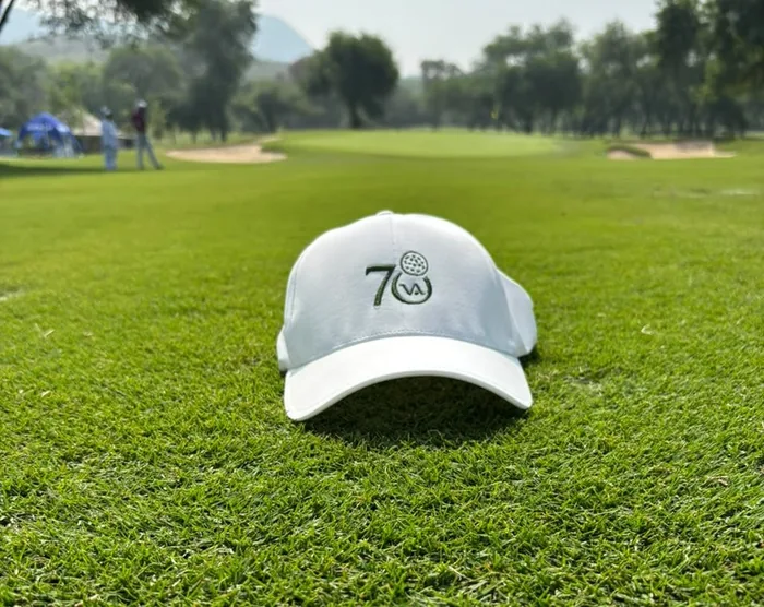 Gorra blanca con número bordado, sobre el pasto de un campo de golf