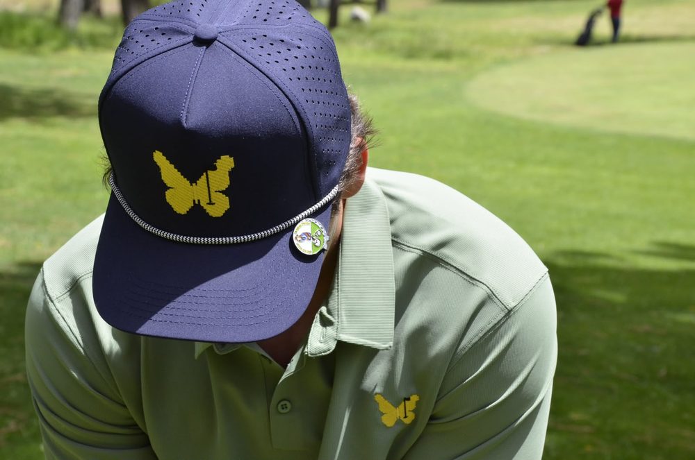 Gorra azul marino con mariposa bordada y polo a juego, en un campo de golf